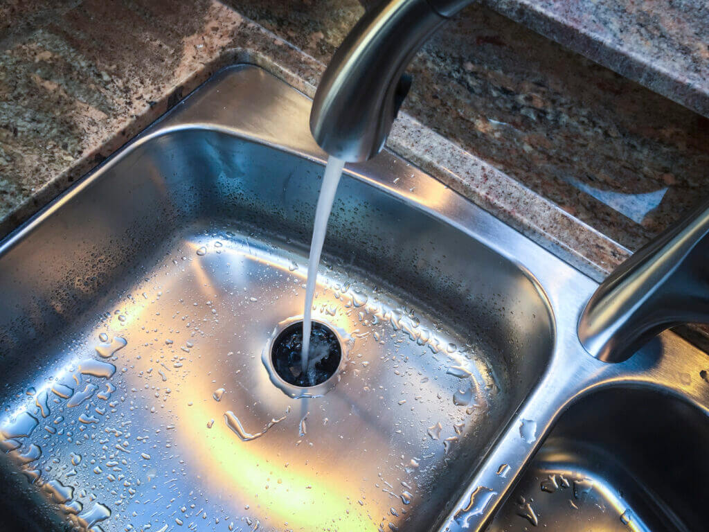 Water going down the drain of kitchen sink with garbage disposal.